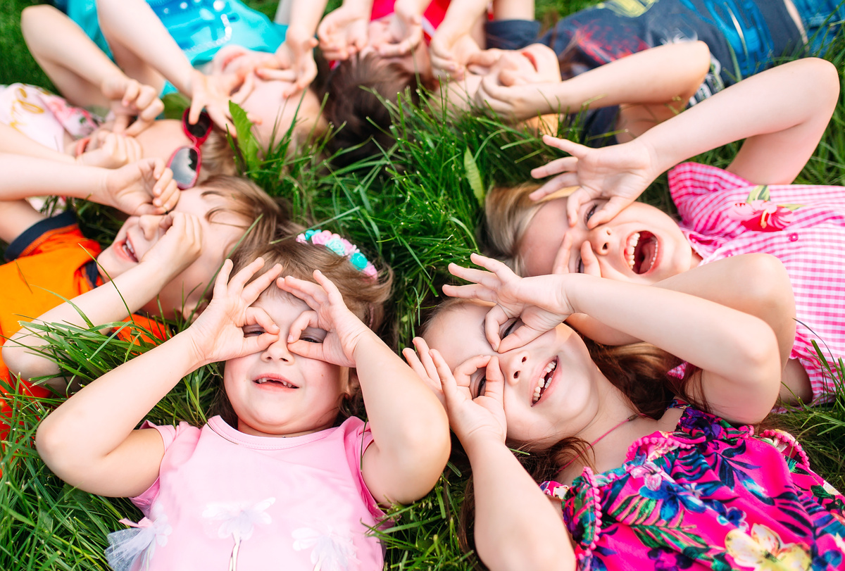 Kids making ok sign on their eyes while lying in grass